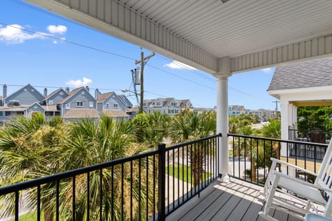 Sway gently in your chair on this covered balcony, where tropical palms frame views of charming coastal homes under endless blue skies.