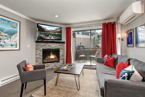 The fantastic living area with its large, flat-screen TV, plush couch that pulls out into a full-size bed, a cozy, modern armchair, roomy coffee table and outdoor patio with mountain village views.
