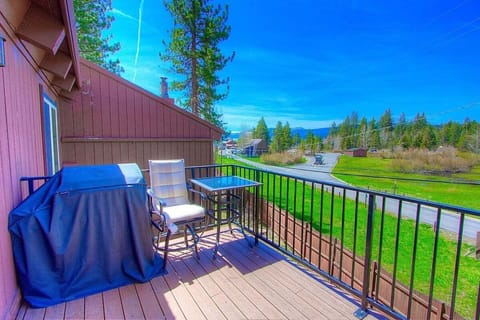 Deck with covered BBQ grill, chair, small table, railing, road, grass, and mountain view.