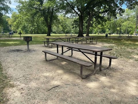 - Picnic tables with built in grills for outdoor meals - Shaded park setting surrounded by tall trees - Perfect spot for family barbecues and group gatherings