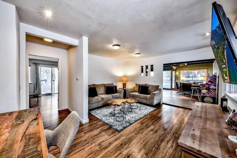 Living room with two beige sofas, wood slab coffee tables, patterned area rug, and wall-mounted TV.