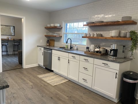 Well stocked kitchen off of office with bright light, open shelving, coffee bar.