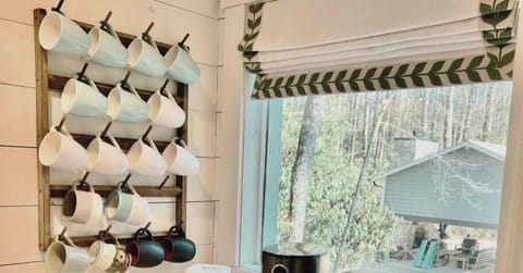 Coffee bar with a variety of mugs and two coffee makers by a window overlooking the woods.