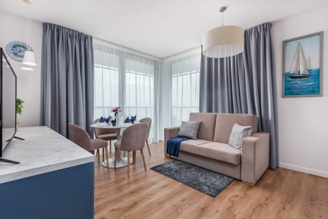 A cozy living room featuring a gray sofa, a matching armchair, and a wooden floor, with a large window providing natural light.