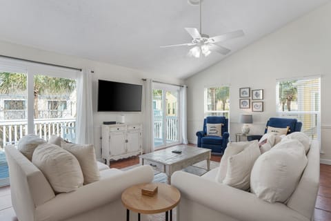 Sink into plush white sofas in your bright, airy living room where coastal breezes flow through large windows and palm trees sway outside.
