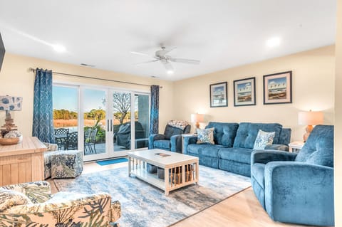Relax in your spacious living room with plush blue seating, coastal decor, and serene views through sliding doors to your private outdoor space.