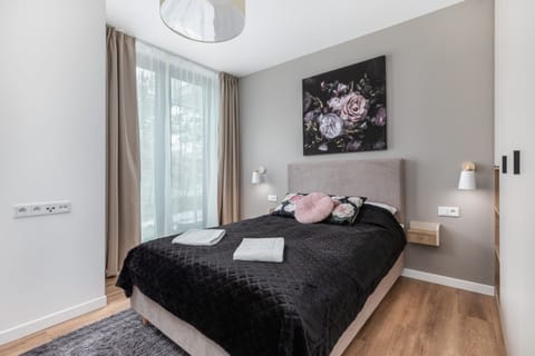 Modern bedroom with double bed with black bedspread. On the wall hangs a painting depicting flowers on a black background.