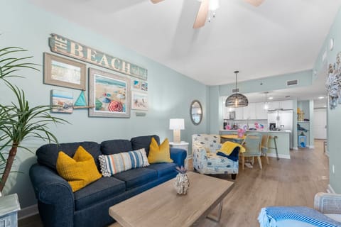 Relax in your coastal-themed living space with beach artwork, comfortable seating, and an open kitchen perfect for vacation dining.
