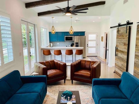 Bright open plan living room with velvet sofas, leather chairs, gold pendant lights and bright kitchen cabinets