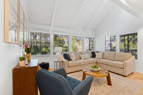 This inviting living room offers a bright, open feel with vaulted shiplap ceilings, warm natural light, and serene views of the surrounding greenery.