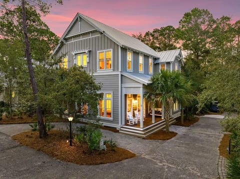 Charming coastal cottage with welcoming front porch and warm evening glow, nestled among lush tropical landscaping.