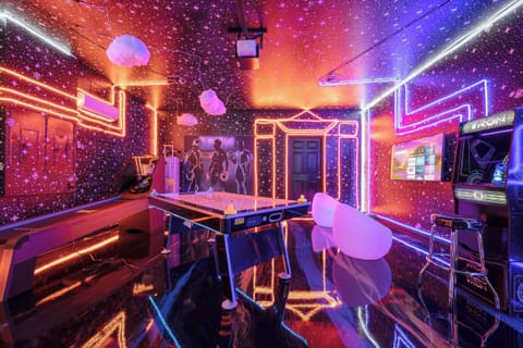 Futuristic neon game lounge featuring a full-size air hockey table, retro arcade games, and a smart TV setup.