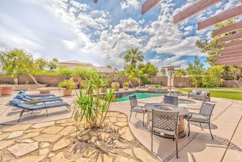 A stone patio, outdoor dining set, lounge chairs, fire pit, lush plants, and a swimming pool all surrounded by a privacy fence.