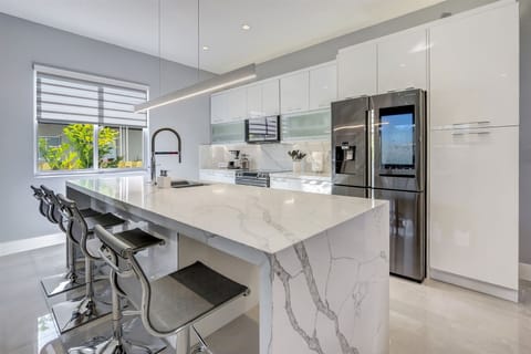 Luxurious kitchen features a white marble, waterfall island -w/ four counter stools-