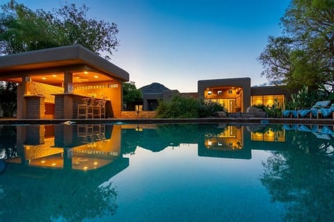 Relax by the illuminated outdoor pool and bar area at sunset in this southwestern-style retreat.
