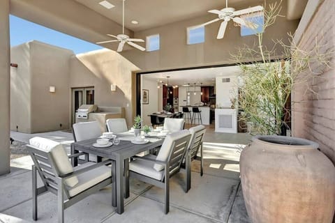 Modern outdoor dining area with comfortable seating and ceiling fans opening to the kitchen.