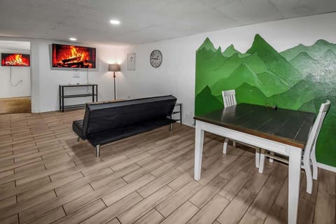 A modern and inviting space featuring a sleek black futon, a stylish coffee table, and a charming dining nook with a green mountain mural accent.