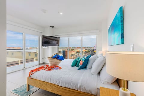 Your bright bedroom features a plush bed with colorful accents, a wall-mounted TV, and sliding doors opening to a balcony with city views.