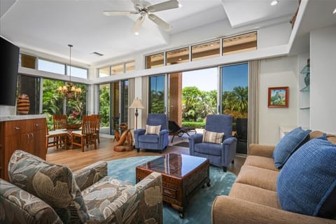 Unwind in your spacious living area with vaulted ceilings, ceiling fan, and floor-to-ceiling windows that open to a lush tropical garden—your bright, breezy retreat awaits.