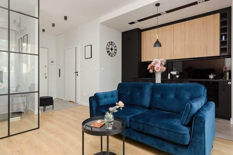 A modern living room with a navy blue sofa, a small round coffee table, and a TV mounted on a wooden accent wall. The space is bright and stylish.