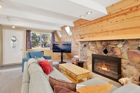 Cozy mountain living room with a stone fireplace, comfy seating, and smart TV—perfect for relaxing evenings, movie nights, and warm cabin vibes after outdoor adventures.