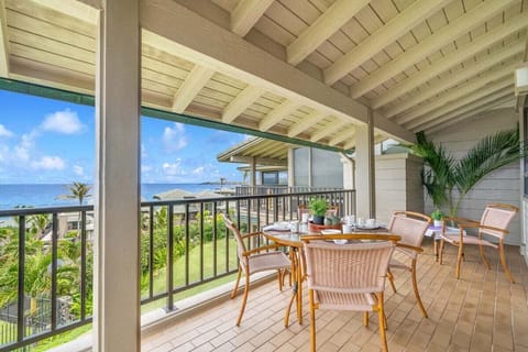 Covered oceanview lanai with a four-seat dining set and ceiling fan, ideal for relaxing meals while overlooking lush tropical greenery and the blue Pacific beyond.