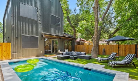 Pool in the backyard that is fitted with turf, outdoor seating, and corn hole