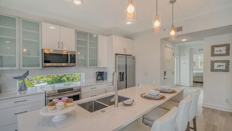 The all-white kitchen gleams with solid surface countertops, sleek cabinetry, and modern lighting.