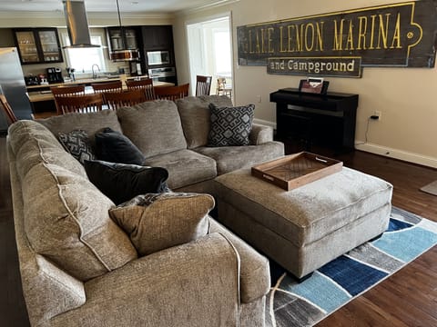 Modern living and dining area with piano, amish-made shaker style dining table, vintage marina sign, and modern kitchen with induction cooktop, vented hood, on island with bar.