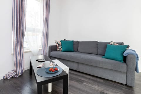 A cozy living room view with gray sofas, teal cushions, a small table, and bright natural light from the windows.