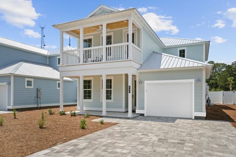 Modern coastal home with distinctive blue siding, covered balcony, and paved driveway in a peaceful residential neighborhood.