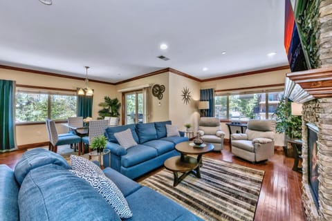 Unwind in this spacious living room with plush blue sofas, cozy fireplace, and abundant natural light streaming through large windows.