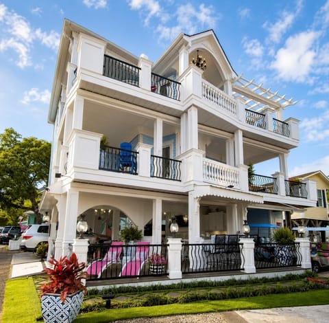 Three-level porch features black iron railings, white columns, pink lounge chairs, and a blue Adirondack chair.