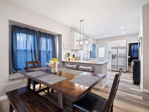 Cozy open space with leather sofas, wooden coffee table, and adjacent dining bench and chairs by bay window. Vinyl plank floors and blue curtains add warmth and style—perfect for relaxing and entertaining! ️️