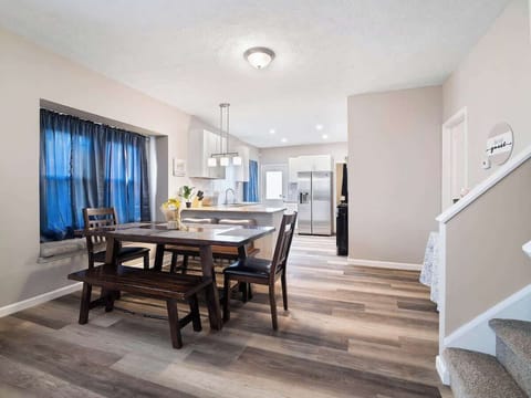 Cozy open space with leather sofas, wooden coffee table, and adjacent dining bench and chairs by bay window. Vinyl plank floors and blue curtains add warmth and style—perfect for relaxing and entertaining! ️️