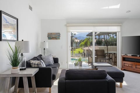 Bright living room with comfy seating, large TV, and balcony views of the pool and mountains.