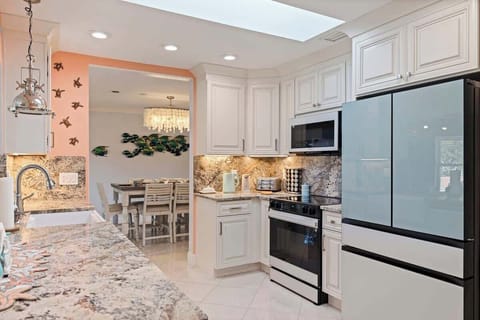 Sunlit coastal kitchen with white cabinetry, granite counters, and modern appliances. A skylight brightens the space, making it perfect for cooking, gathering, and sharing meals after a day on the water.
