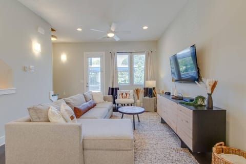 Bright and inviting living room with a plush sectional sofa, flat-screen TV, ceiling fan, and large windows letting in natural light.