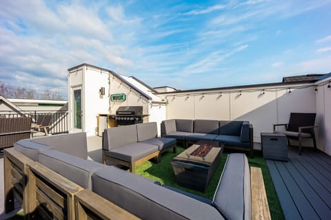 Stunning rooftop deck with multiple lounge areas, fire pit, smart TV, BBQ grill, and dining area.
