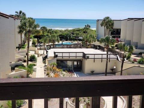View from the balcony featuring lush gardens, a sparkling pool, and the ocean.