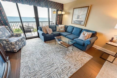 - Spacious oceanfront living room with a cozy sectional, perfect for unwinding - Floor to ceiling windows open to a private balcony, bringing in fresh sea breezes - Coastal inspired décor and a soft area rug add warmth and comfort to this inviting sp