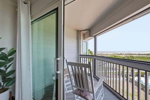 Screened porch with white rocking chairs overlooking dunes and ocean beyond the black railing.