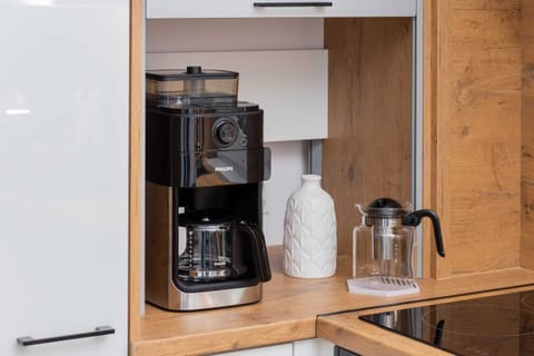 A coffee machine and various accessories, including cups and a kettle, displayed on a wooden countertop.