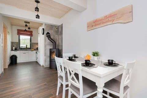 A living and dining area featuring a white dining table with chairs, a wood-burning fireplace, and large windows.