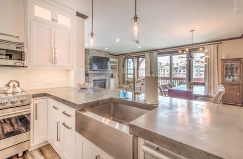 - Bright kitchen overlooking the living room with scenic window views - Stone counters, farmhouse sink, and warm lighting enhance the space - Ideal for après-ski cooking, casual gathering, and cozy mountain living