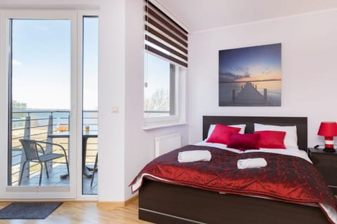 Bright bedroom with a red and white color scheme, large windows, and a cozy double bed.
