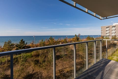 A balcony with a small outdoor table and chairs overlooks a beautiful sea view. Glass railings provide unobstructed vistas, creating a peaceful space to relax.