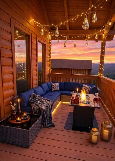 Covered deck with outdoor sofa — string lights, fire feature, and mountain sunset views