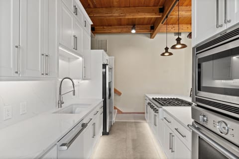 Step into your gourmet galley kitchen where sleek white cabinetry meets rustic wooden beams overhead. You'll love cooking with professional-grade appliances while pendant lights cast a warm glow above.