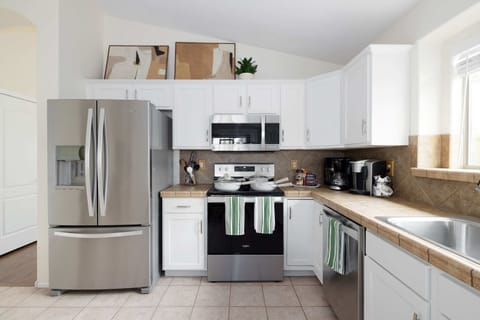 Modern kitchen with stainless steel appliances, white cabinetry, and tiled countertops.